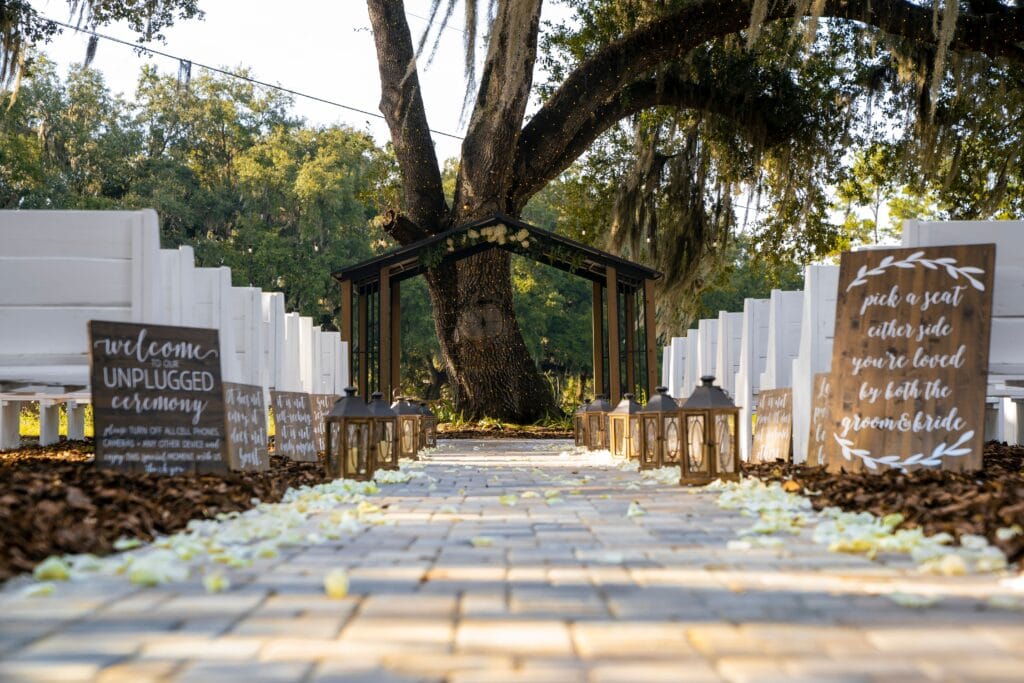 outdoor wedding ceremony with wood signs, white benches, and lanterns