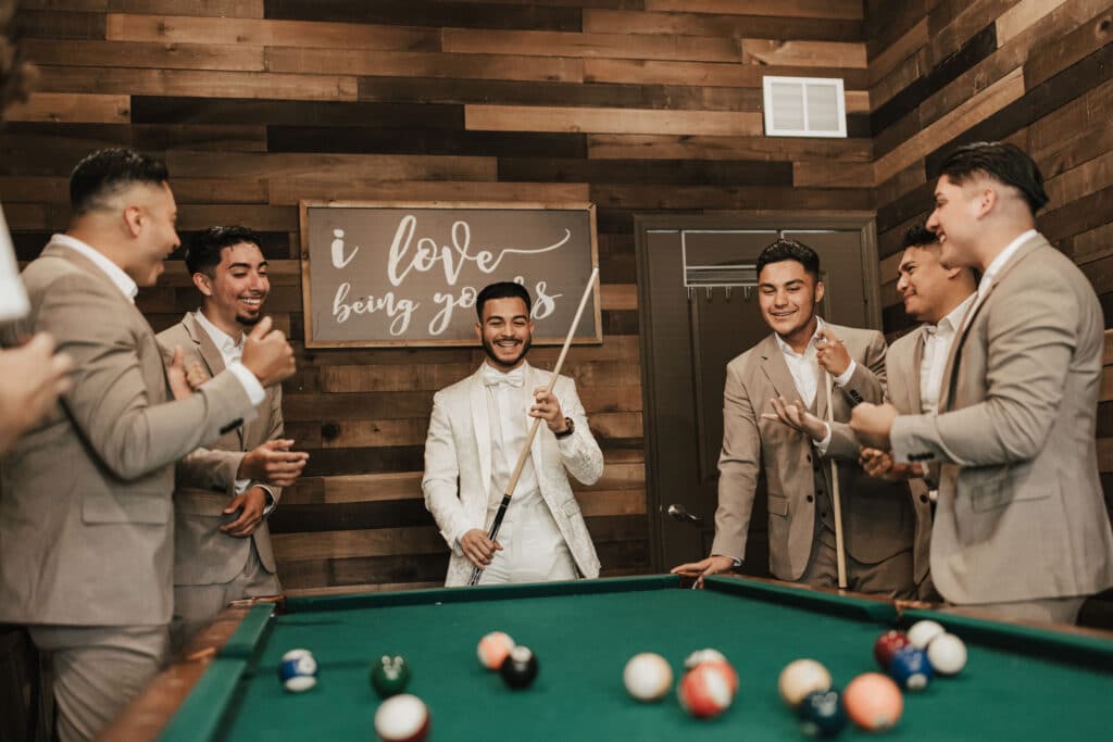 groom and groomsmen playing pool in room with wood walls