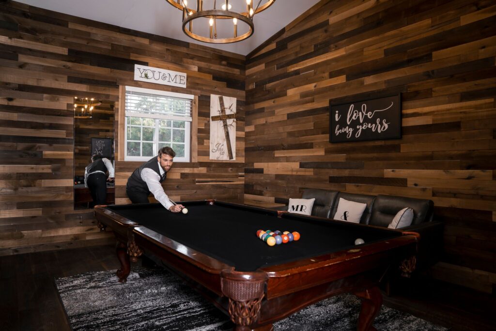 groom playing pool in a room with wood panel walls and dark furniture
