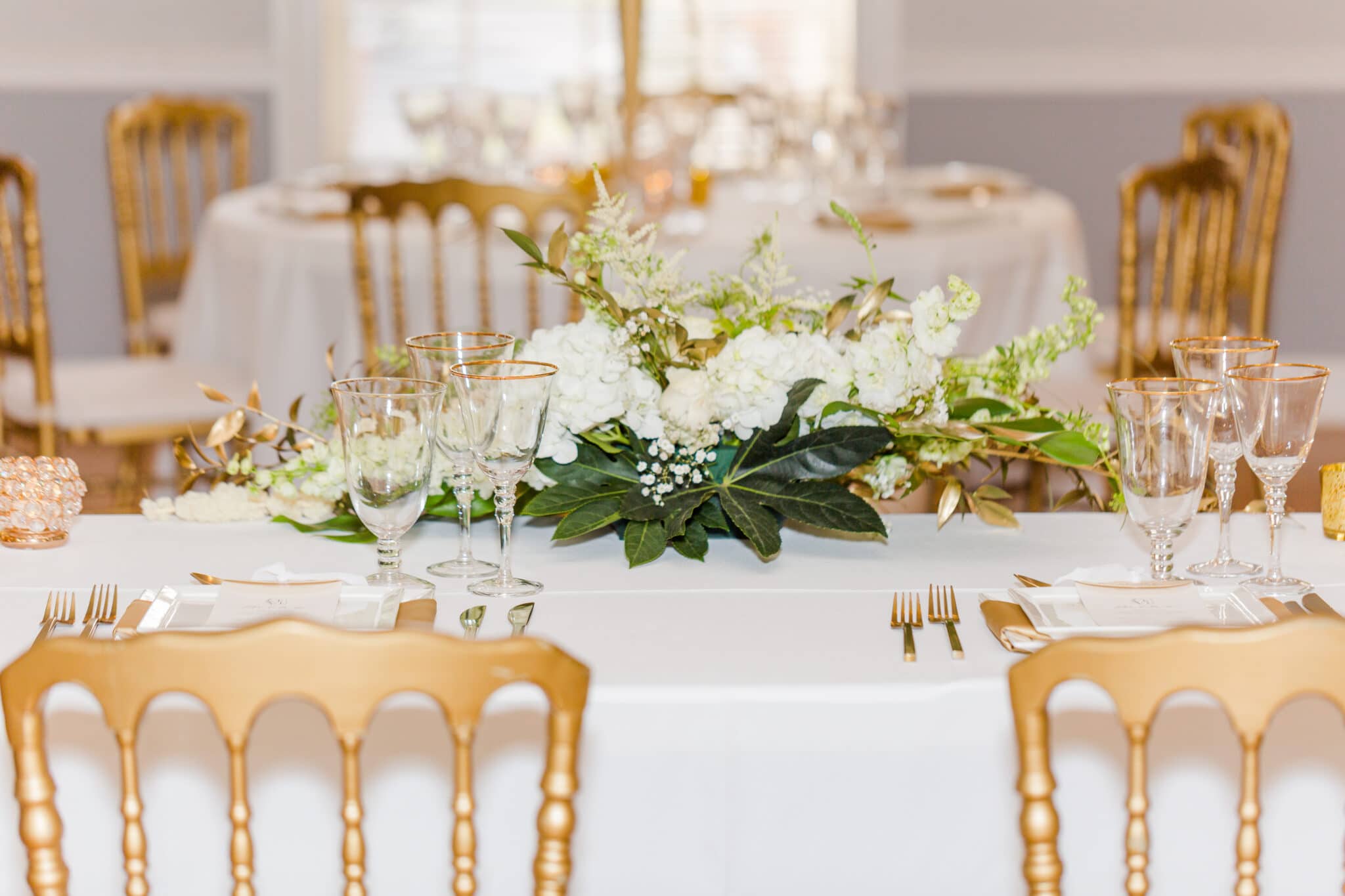 the flower arrangement and gold rimmed glasses on the sweetheart table