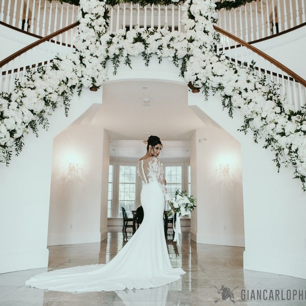 bride below staircase with white flowers in arch above by Flowers by Lesley
