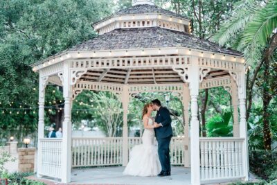 Bride and groom kissing under a white gazebo amongst trees