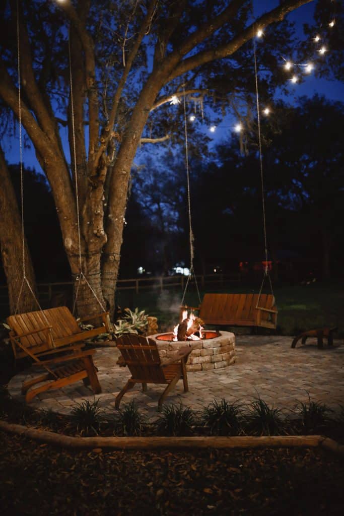 stone firepit, surrounded by wooden benches, adirondack chairs, stone walkway, under a tree, twinkle lights, Central FL