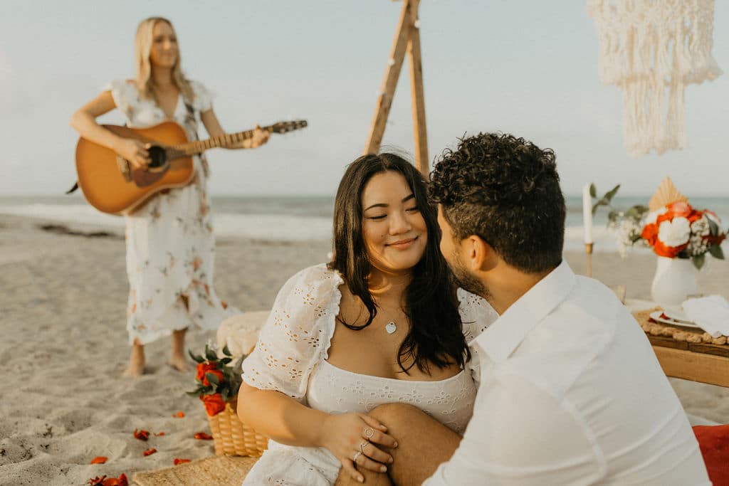 couple smiling on beach with woman playing guitar in background