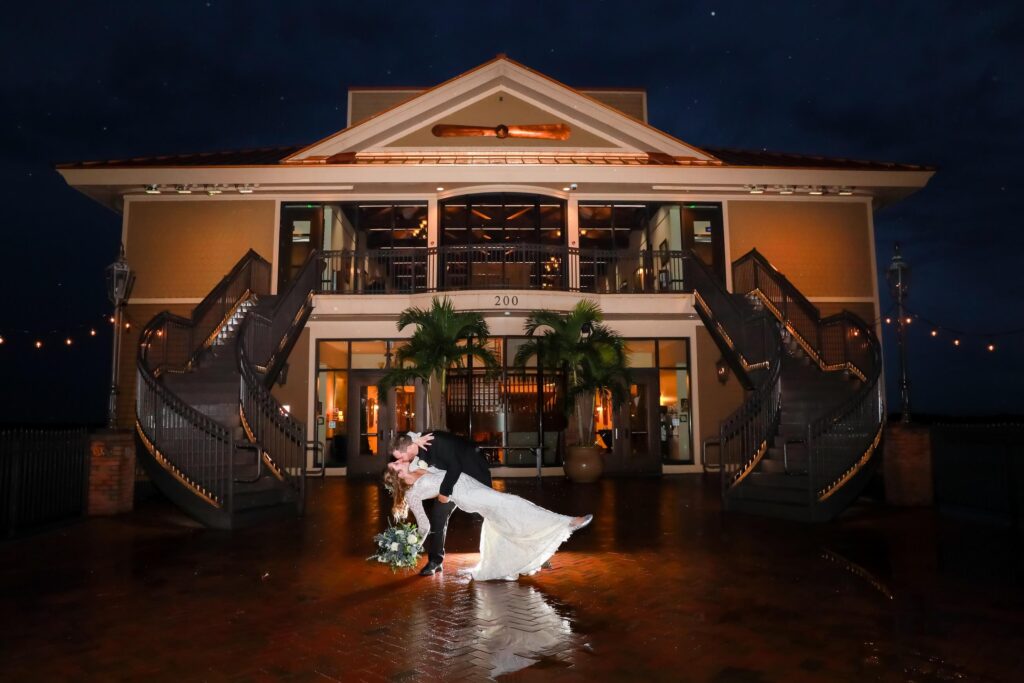 Groom dipping his bride while kissing her in front of their venue