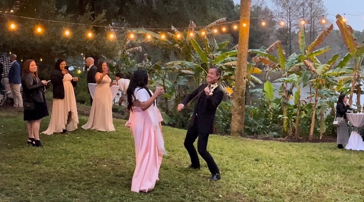 Man and woman dancing at a wedding. They are outside and the woman is wearing a pink dress