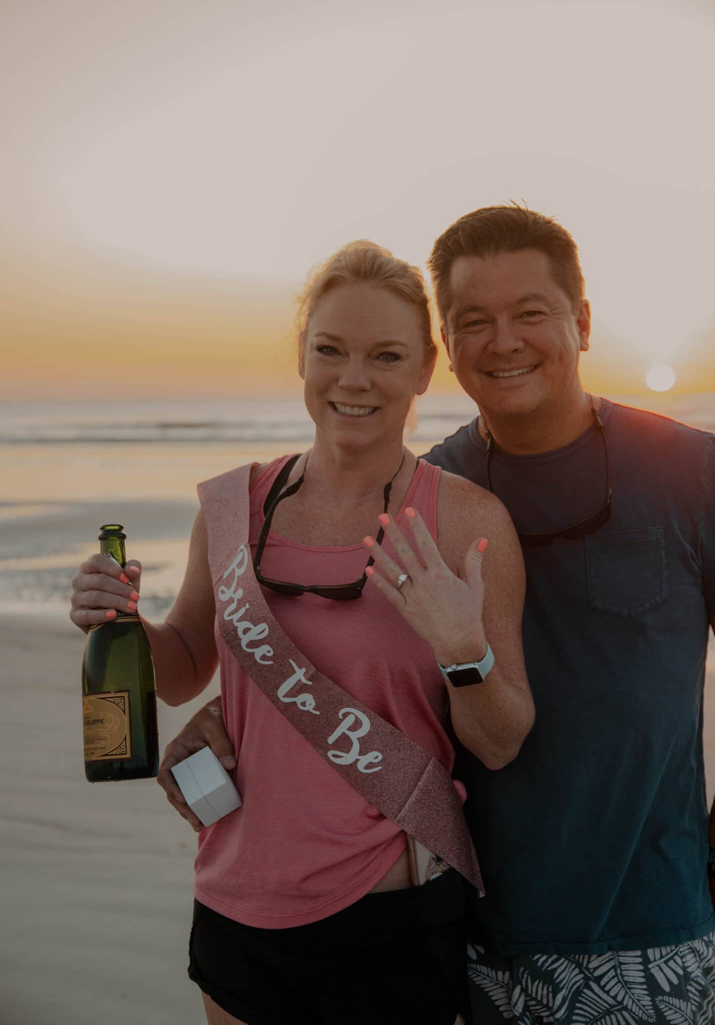 Couple celebrating marriage proposal on sunrise beach with champagne