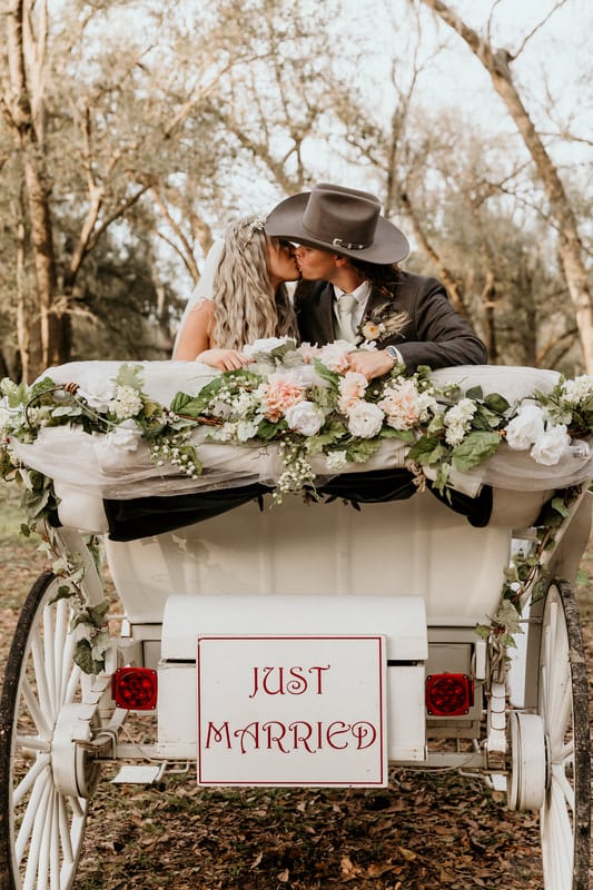 couple kissing in the white wooden wagon, adorned with pink and white flowers, Just Married sign, Still Creek Farm, Central FL