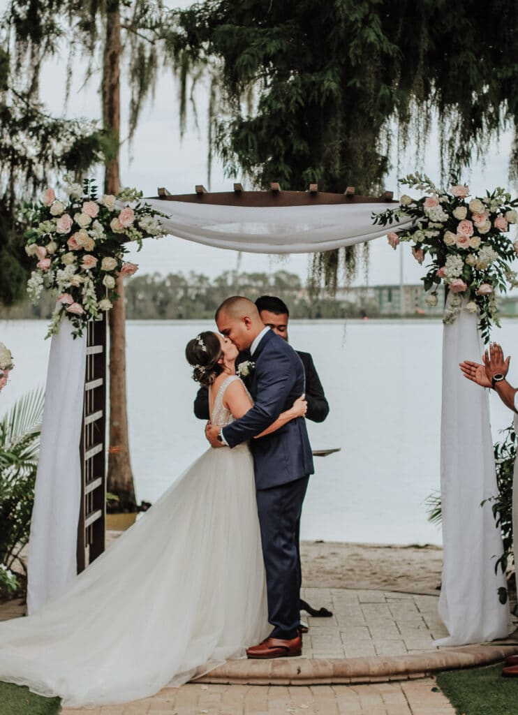 bride and groom kissing under wedding altar at an outdoor wedding with a lake in the distance photo by Carolina Irais Photography