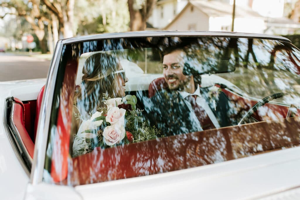 bride and groom in convertible smiling at each other by Joanna Moore Photography