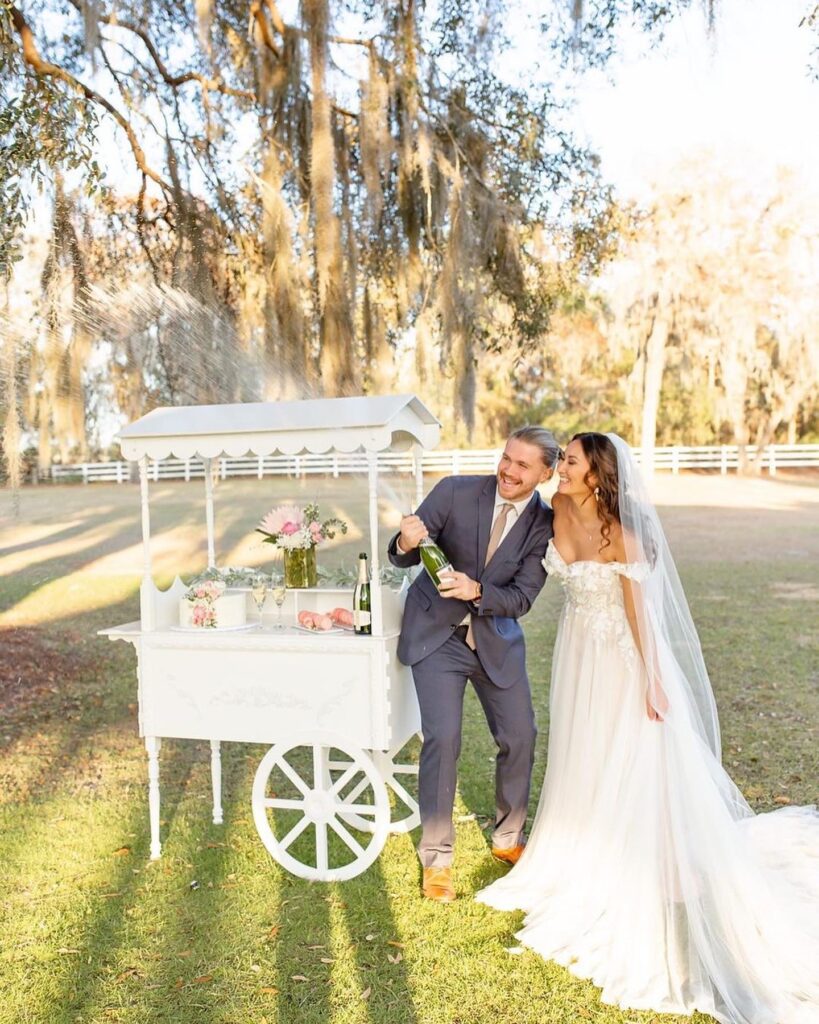 bride and groom in front of white wedding wagon with desserts