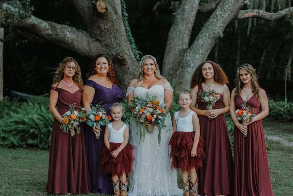 Bride with maid of honor in purple and brides maids in burgandy, flower girls in cowboy boots photo by Carolina Irais Photography