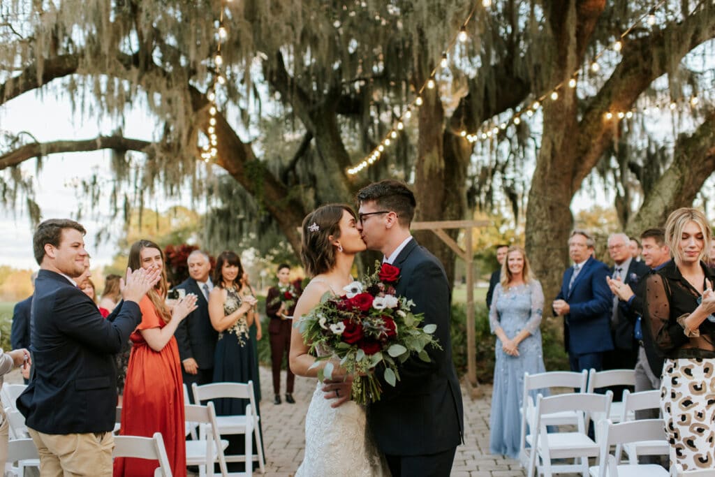 bride and groom kissing in the aisle under market lights and Spanish moss by Joanna Moore Photography