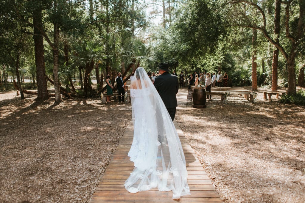 bride and groom walking down brick path in forest by Joanna Moore Photography