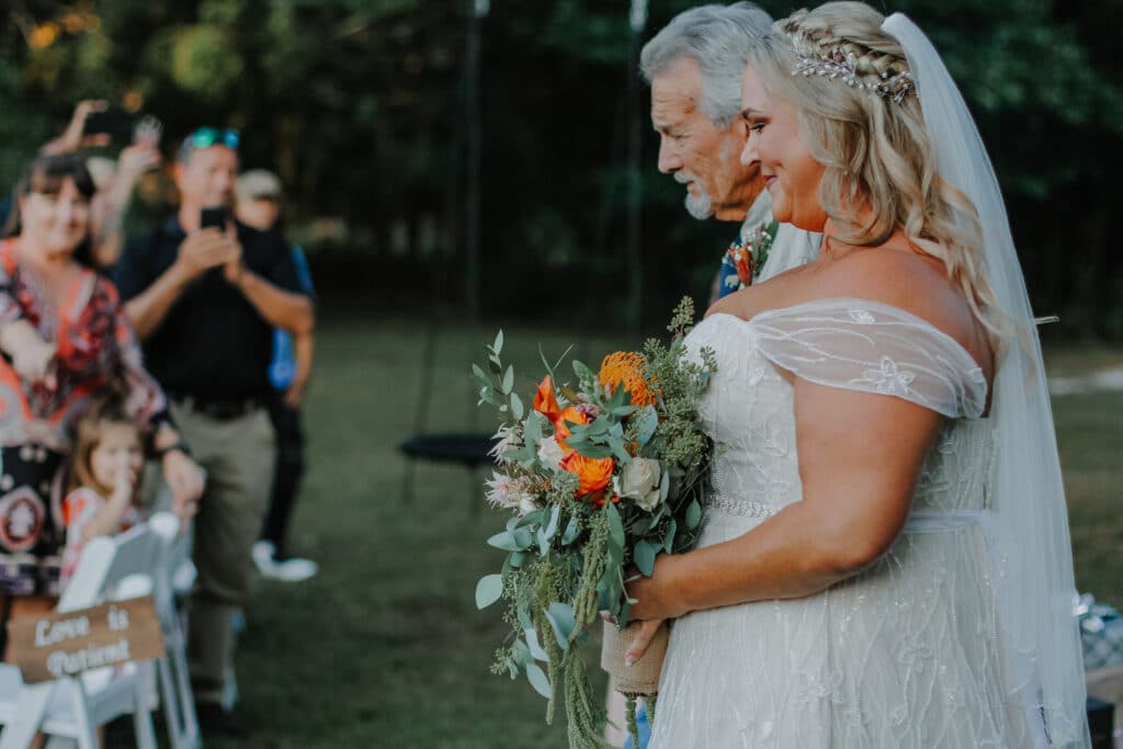 photo by Carolina Irais Photography of bride with orange roses in her bouquet walking down the aisle with her father