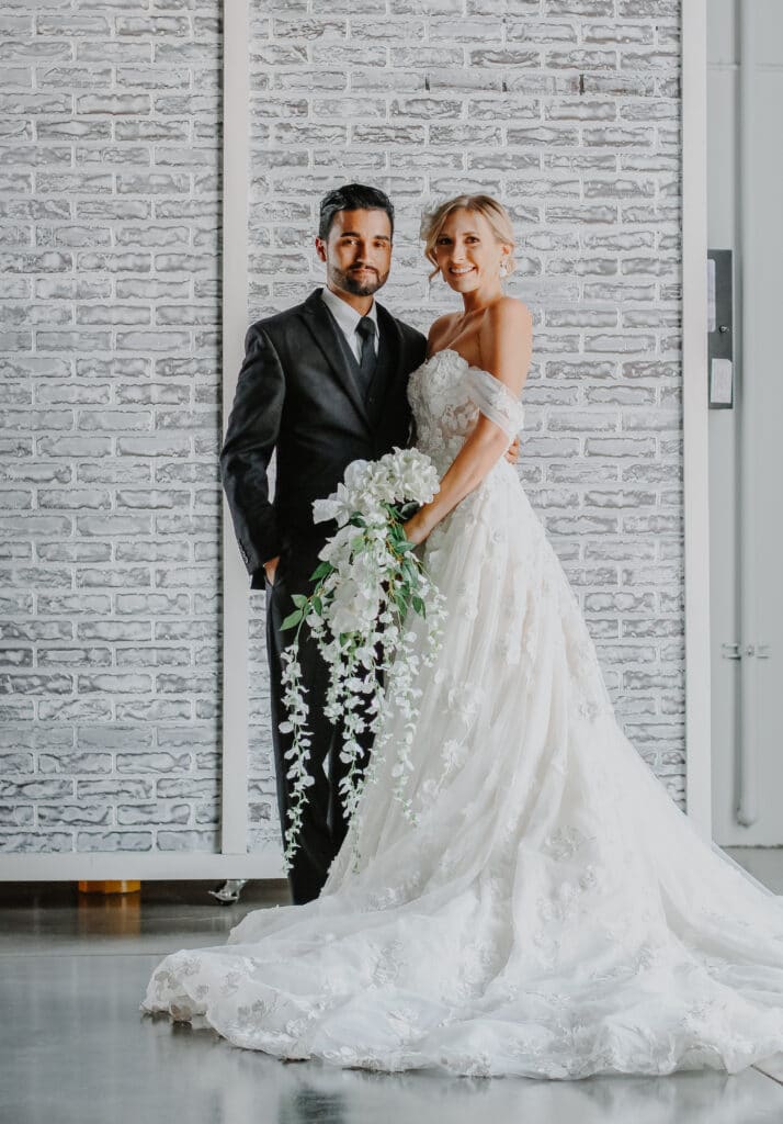 bride and groom smiling in industrial wedding venue with white brick backdrop at D'Space Orlando