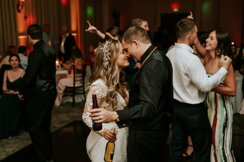 bride and groom dancing and smiling holding beer bottles on dance floor by Joanna Moore Photography
