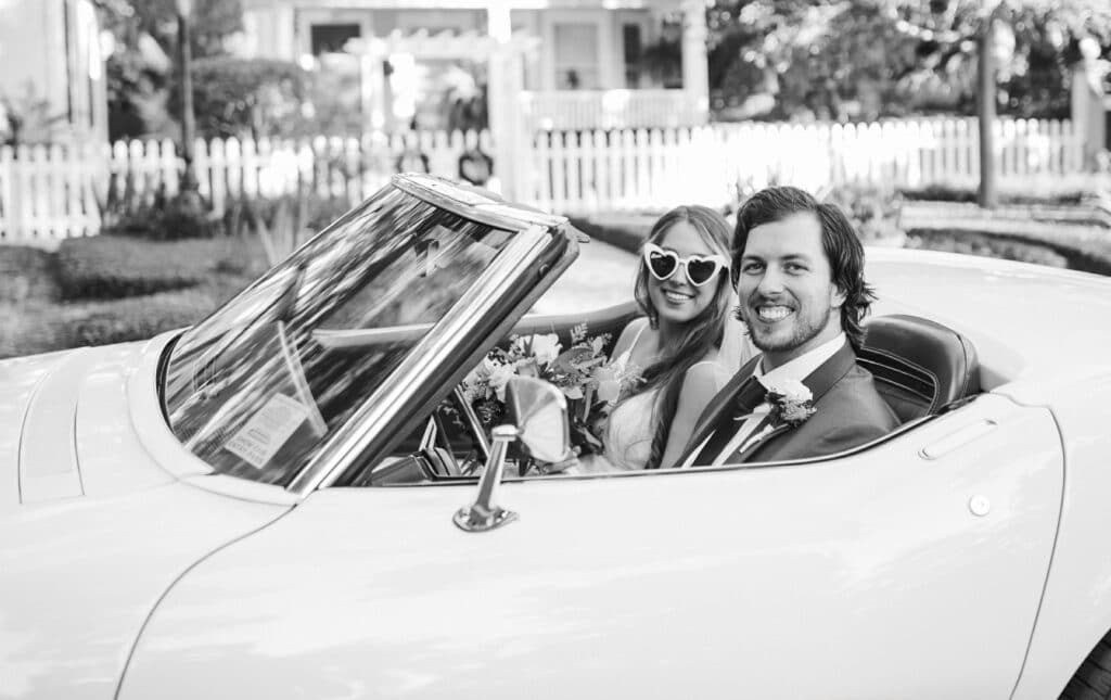 black and white photo of bride with sunglasses and groom in convertible by Joanna Moore Photography