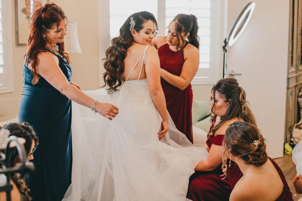 Mother of the bride and bridesmaids helping a bride with her dress