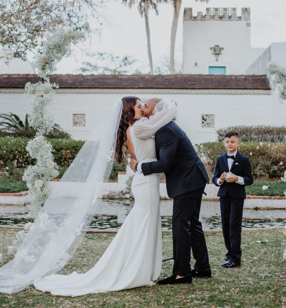 bride and groom kissing in an outdoor ceremony with ring bearer watching photo by Carolina Irais Photography