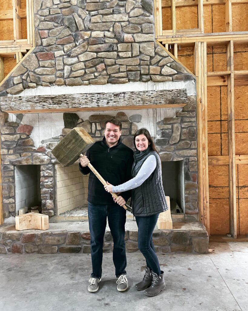 couple holding large wooden mallet in front of stone fireplace at The Sugar Barn at Flying Osceola Ranch