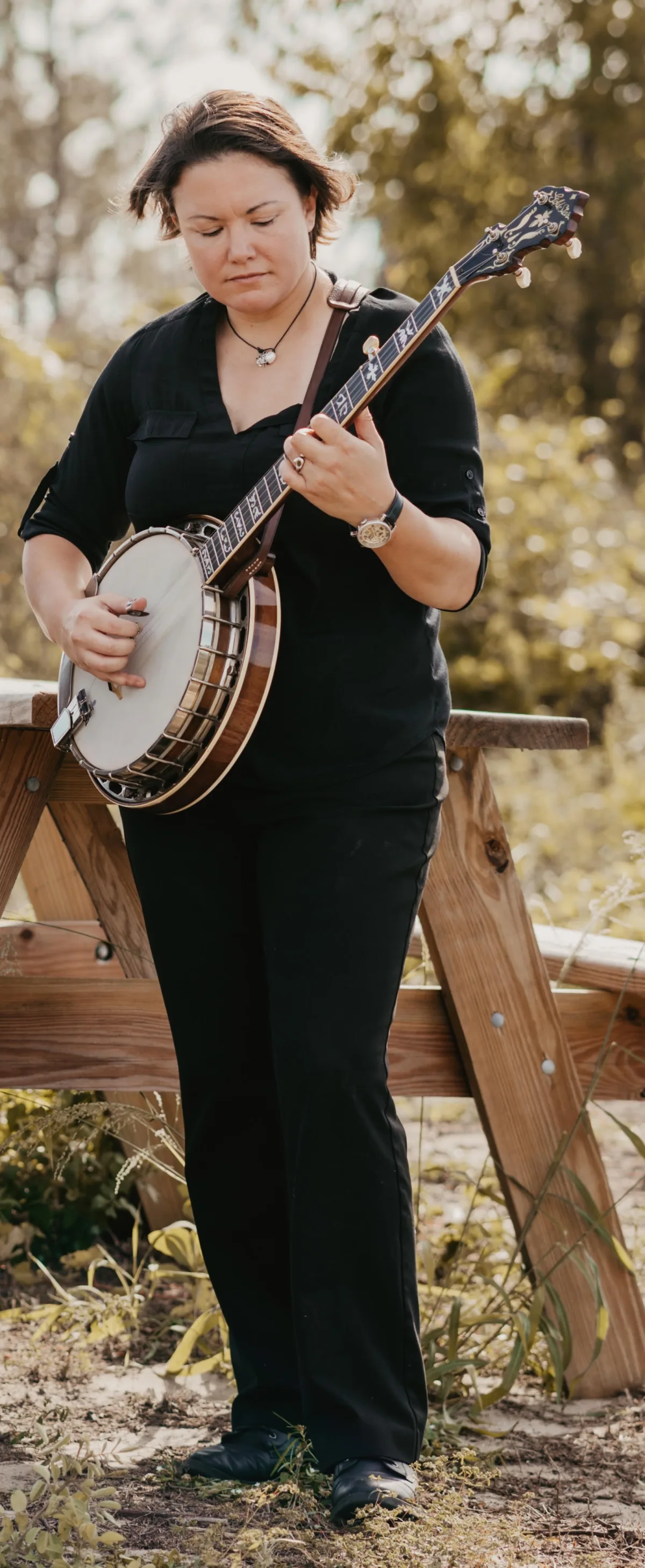 female banjo musician playing outdoors near a wooden fence surrounded by greenery, performed by Aloha Musicians for a Central Florida wedding