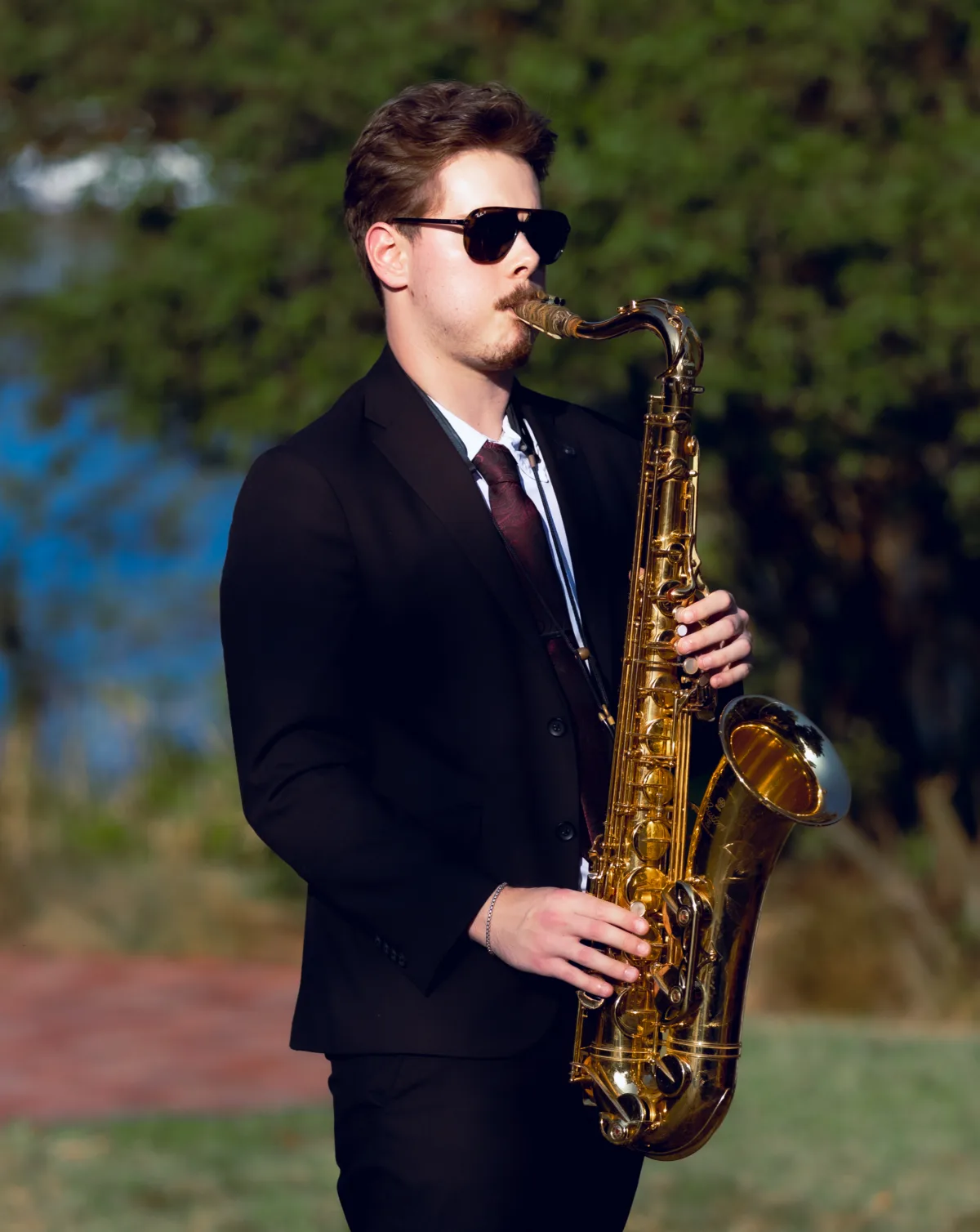 saxophonist in a black suit and sunglasses playing a gold saxophone outdoors at a Central Florida wedding, performed by Aloha Musicians based in Orlando Florida
