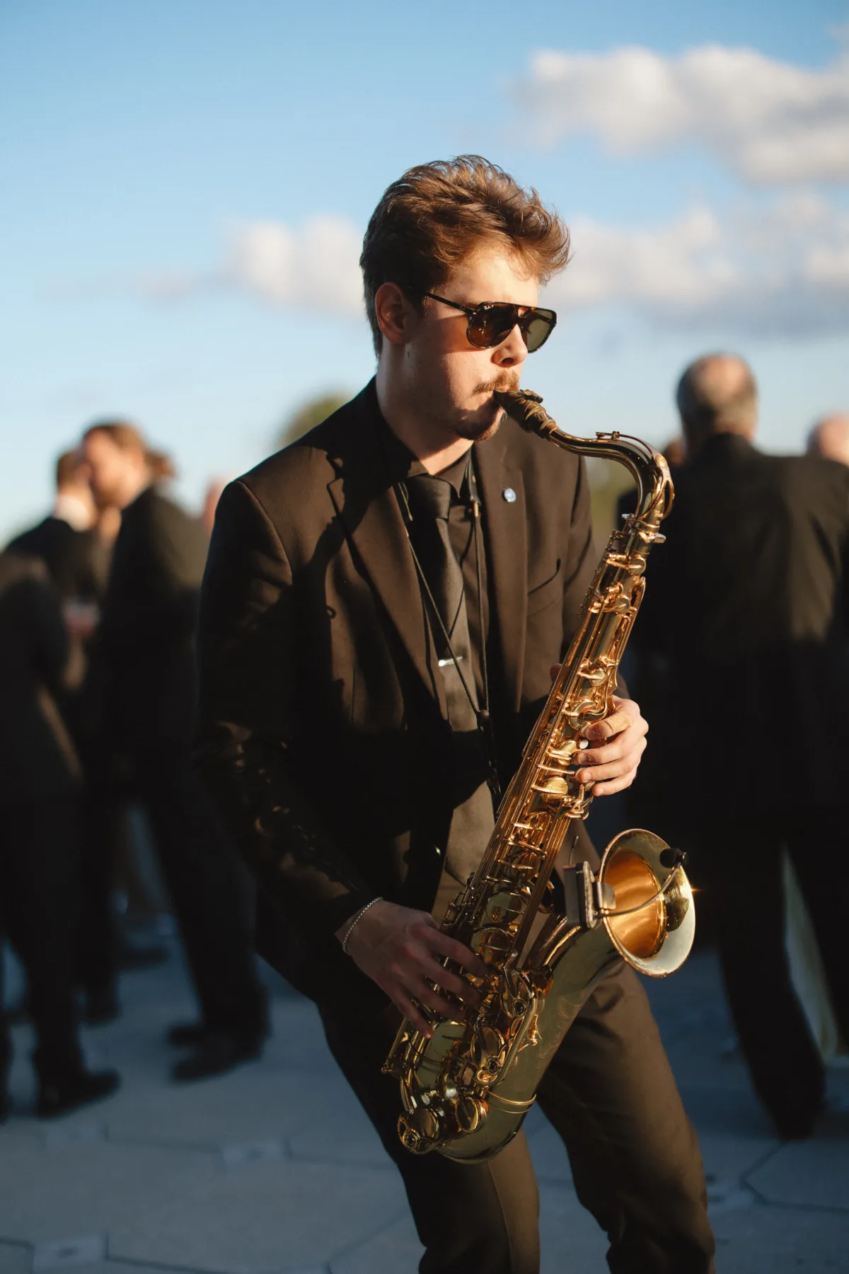 saxophonist in black suit and sunglasses playing a gold saxophone outdoors at a golden hour wedding reception in Orlando Florida performed by Aloha Musicians