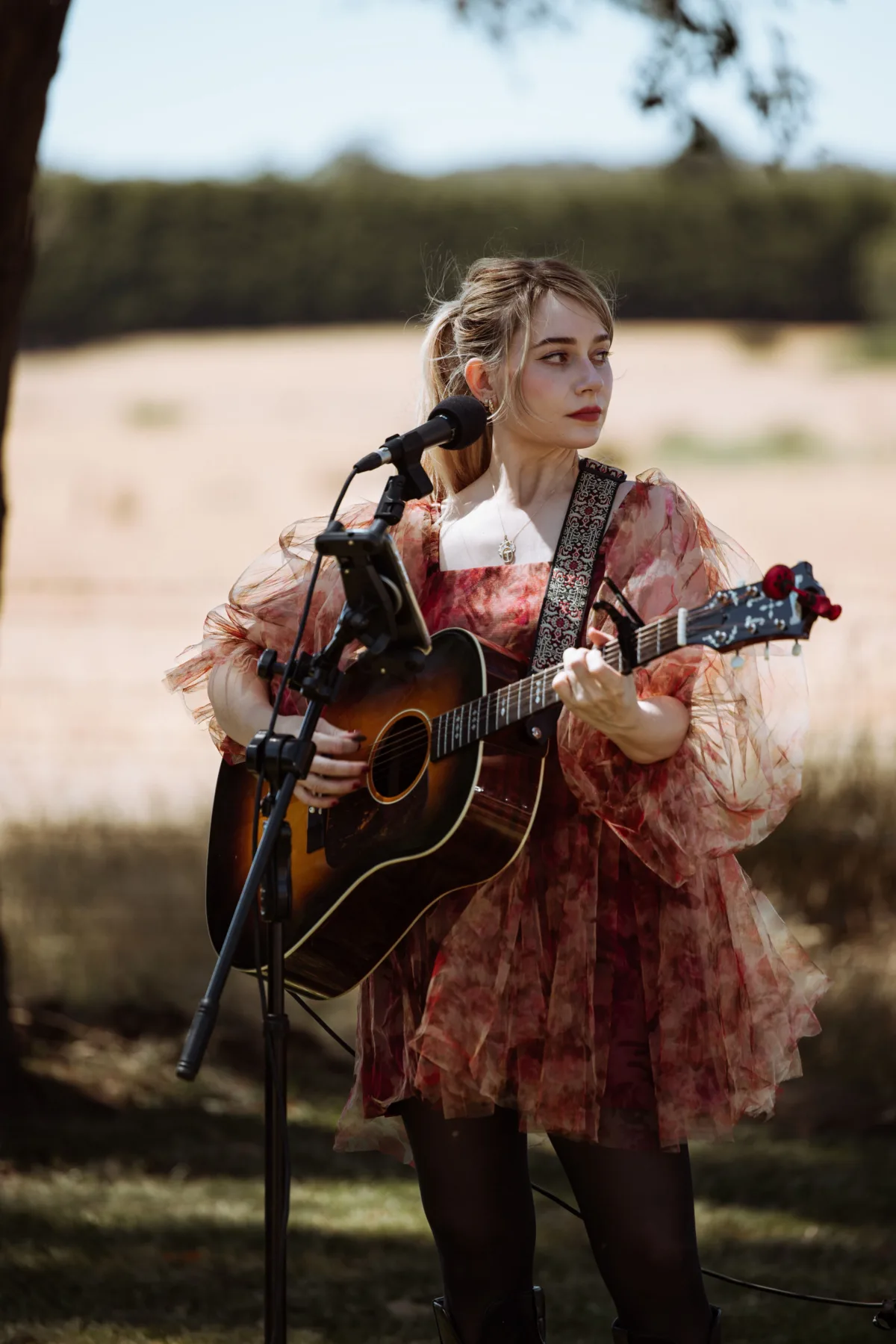 female musician playing acoustic guitar at outdoor microphone stand wearing a floral organza dress performing live at a Central Florida wedding, provided by Aloha Musicians