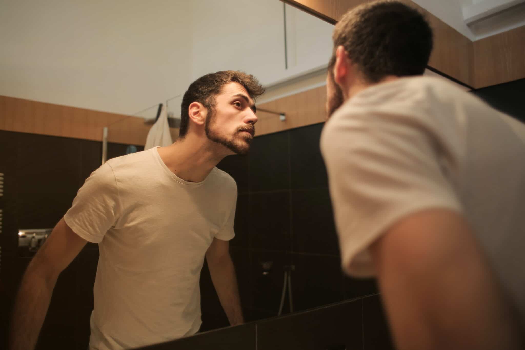 man looking at his reflection in a mirror checking his beard cut for Essential Pre-Wedding Grooming Treatments
