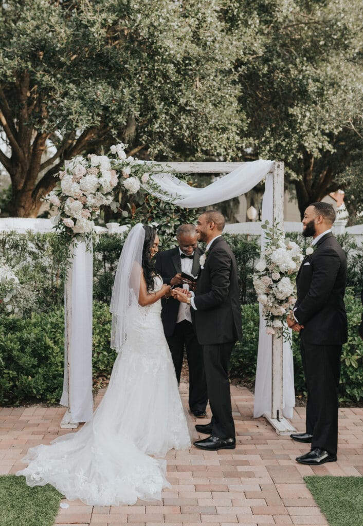 Bride and groom exchanging vows near wooden arch adorned with flowers