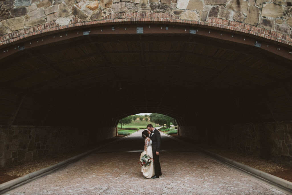 bride and groom kissing under stone arch entrance to tunnel photo by Rudy and Marta Photography