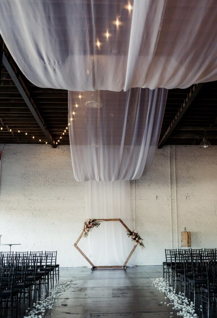 large room set up as a wedding with white draping and seating