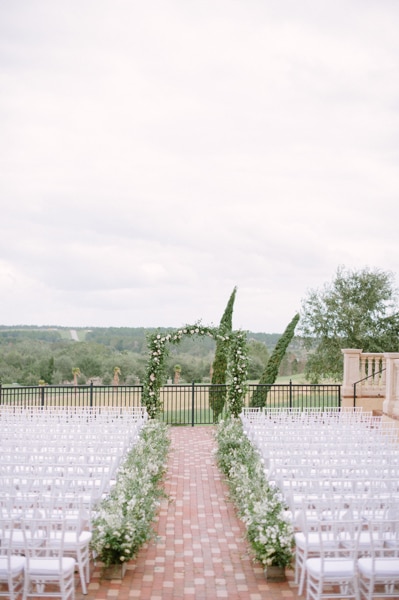 Outdoor ceremony set up with flowers and an arch. Adorned with white chairs