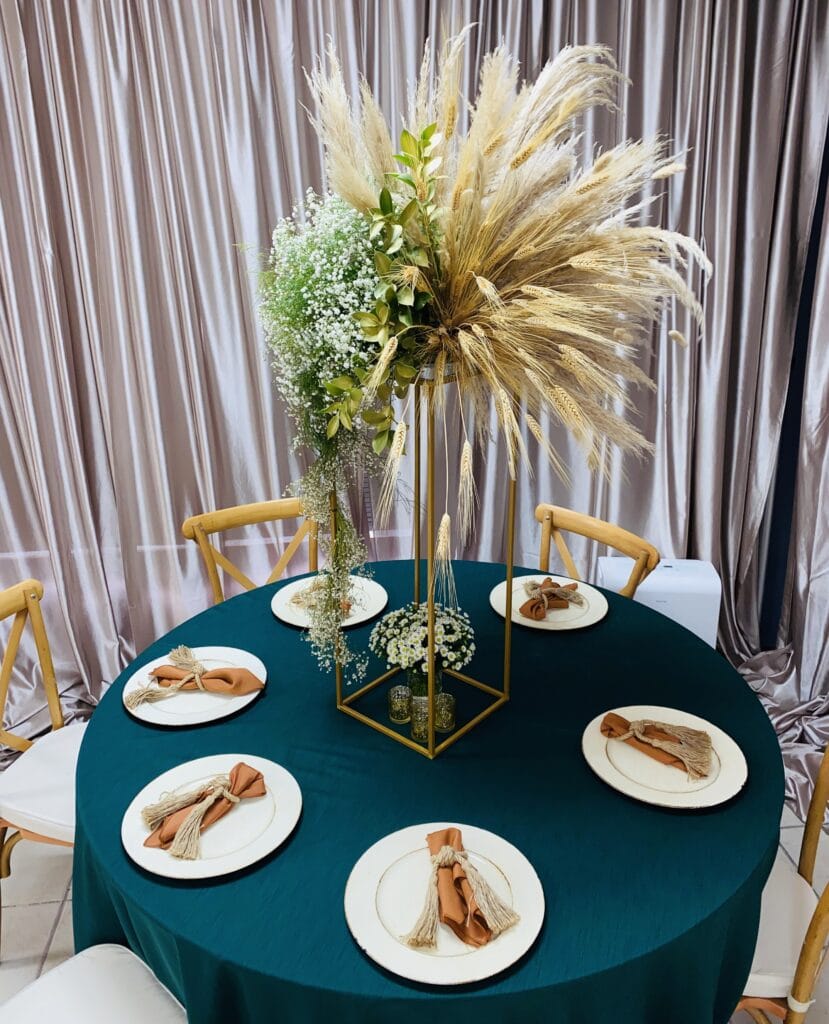 teal tablecloth with tall centerpiece of wheat fronds and green leaves by Stems in Bloom