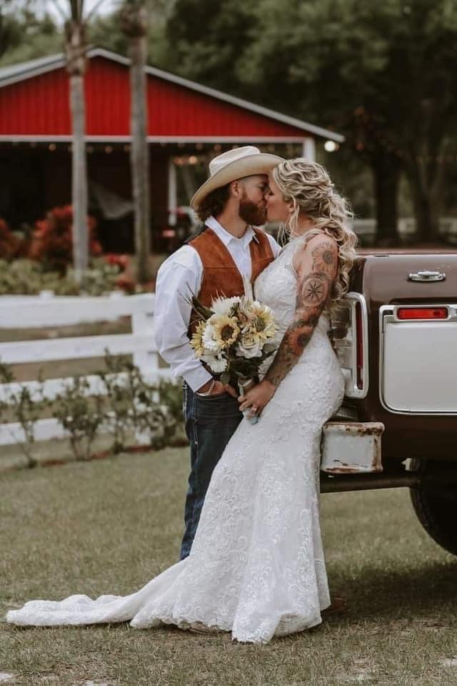 Bride and groom kissing against the back of their truck. She has is holding her bouquet.