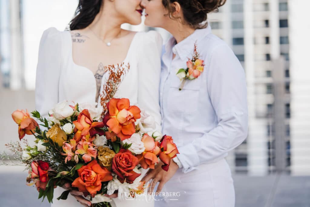 Brides kissing after their ceremony. One woman is holding a bouquet of rust colored flowers