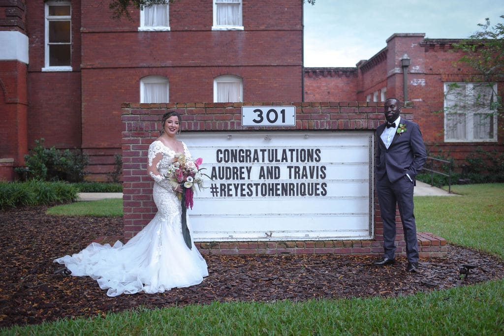 Bride and groom standing in front of a sign that reads 'Congratulations Audrey and Travis'