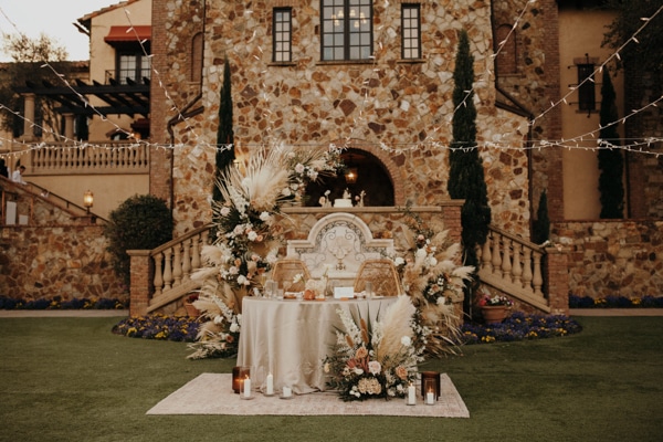 Outdoor bridal table under twinkle lights in front of a stone building