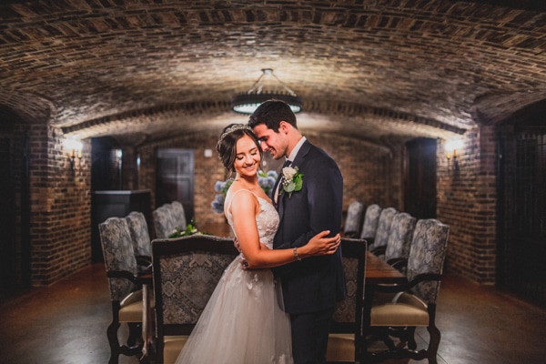Bride and groom under a brick ceiling. They are embracing and smiling