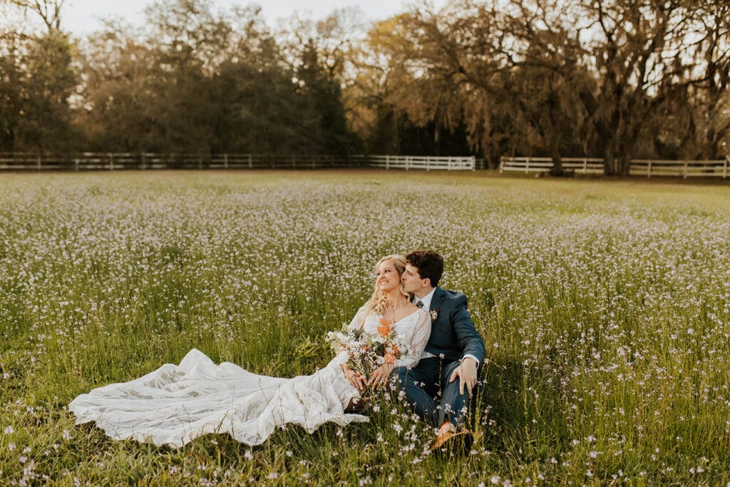 bride and groom sit in a field of flowers at Bramble Tree Estate