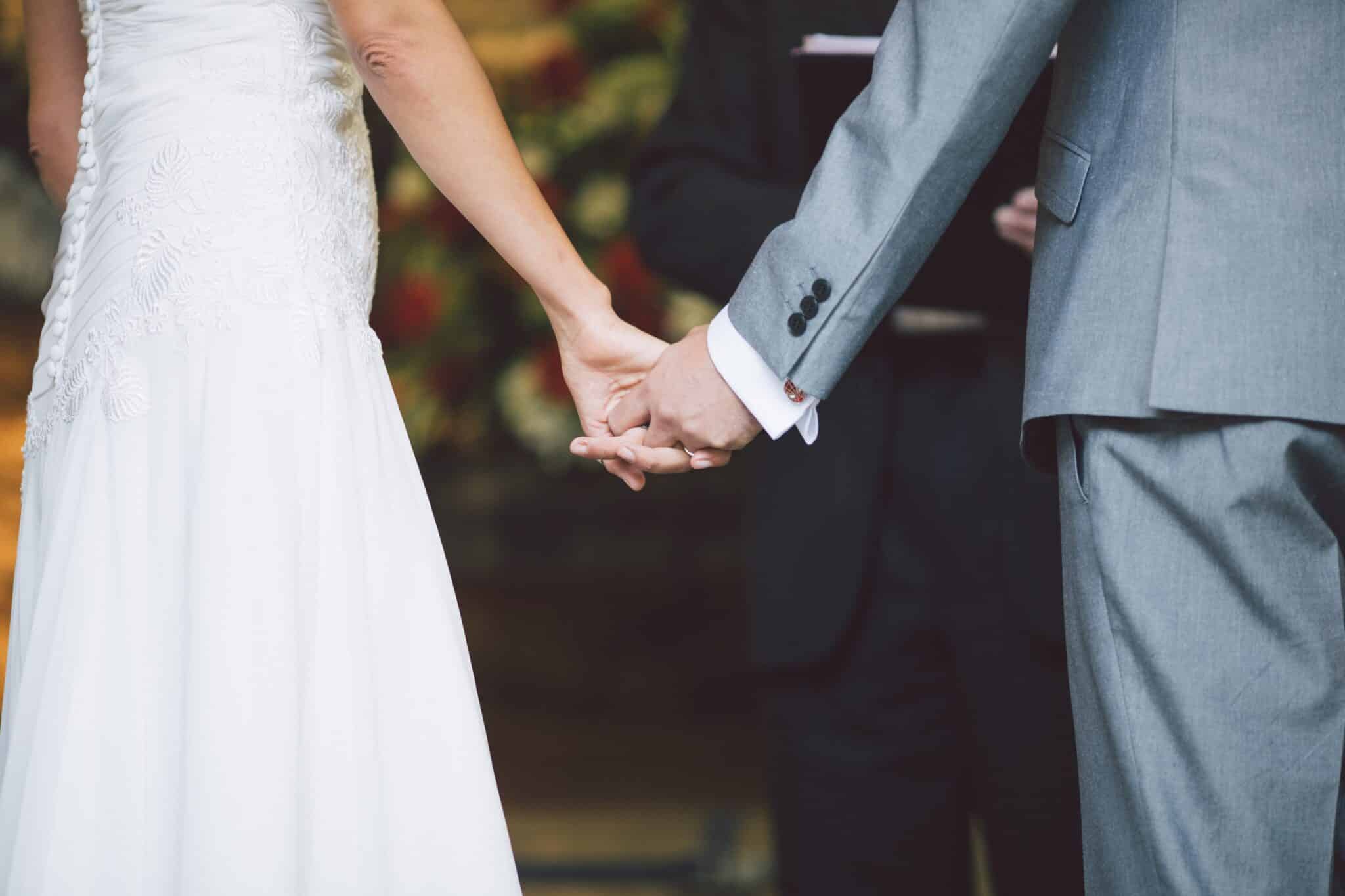 bride in white dress and groom in grey suit holding hands while using a wedding ceremony outline for their ceremony