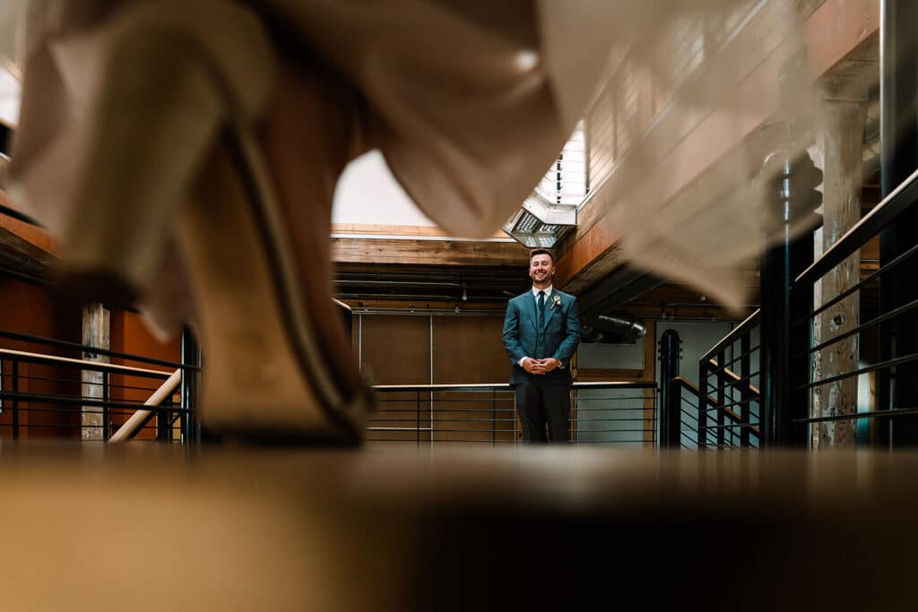 groom waiting for bride as bride comes down the stairs by Roy Serafin Photo Company