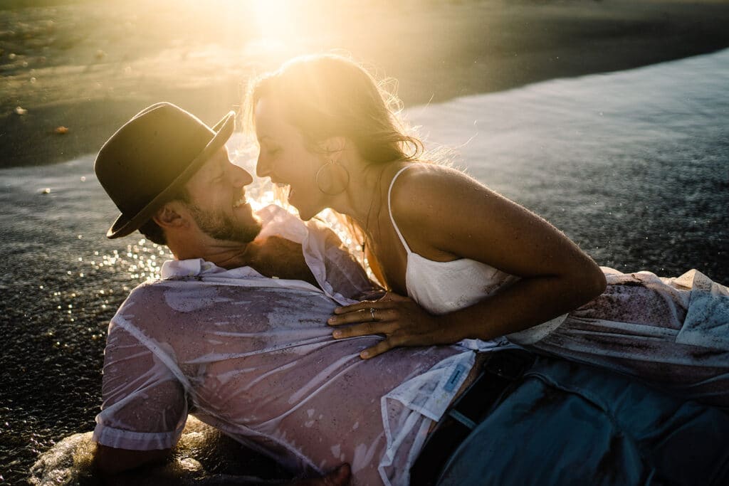bride and groom in a hat rolling in the waves at sunset by Roy Serafin Photo Company