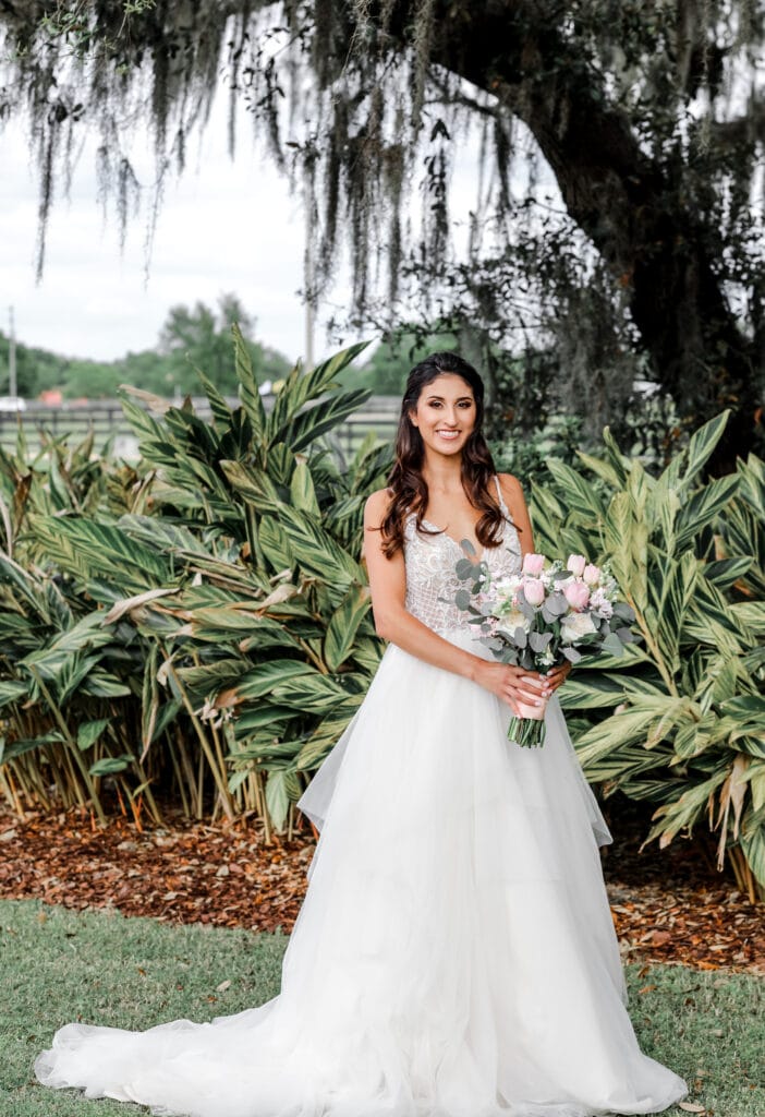 bride in dress with tulle skirt by Enchanted Bride stands under oaks with Spanish moss and palm fronds in background