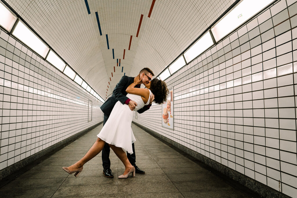 man bending woman over his arm and kissing her in subway tunnel by Roy Serafin Photo Company
