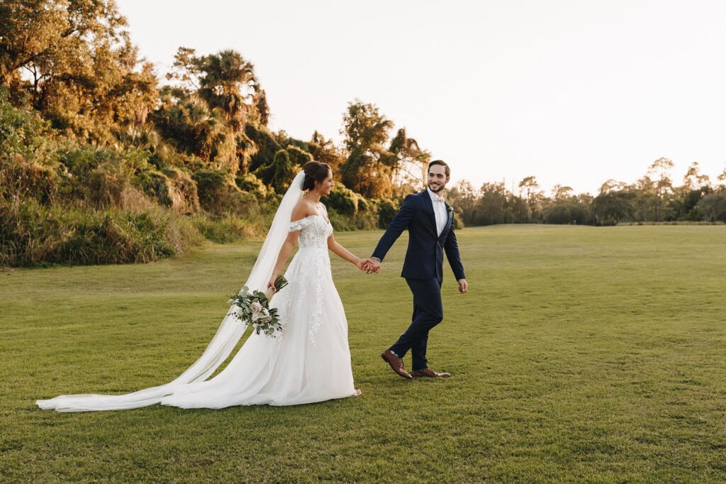 groom leads bride in wedding dress from Enchanted Bride across a field