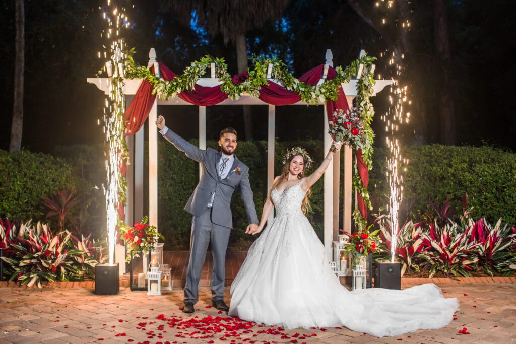 bride and groom posing for photo with hands raised, lights and flowers, details by 360 Emotions