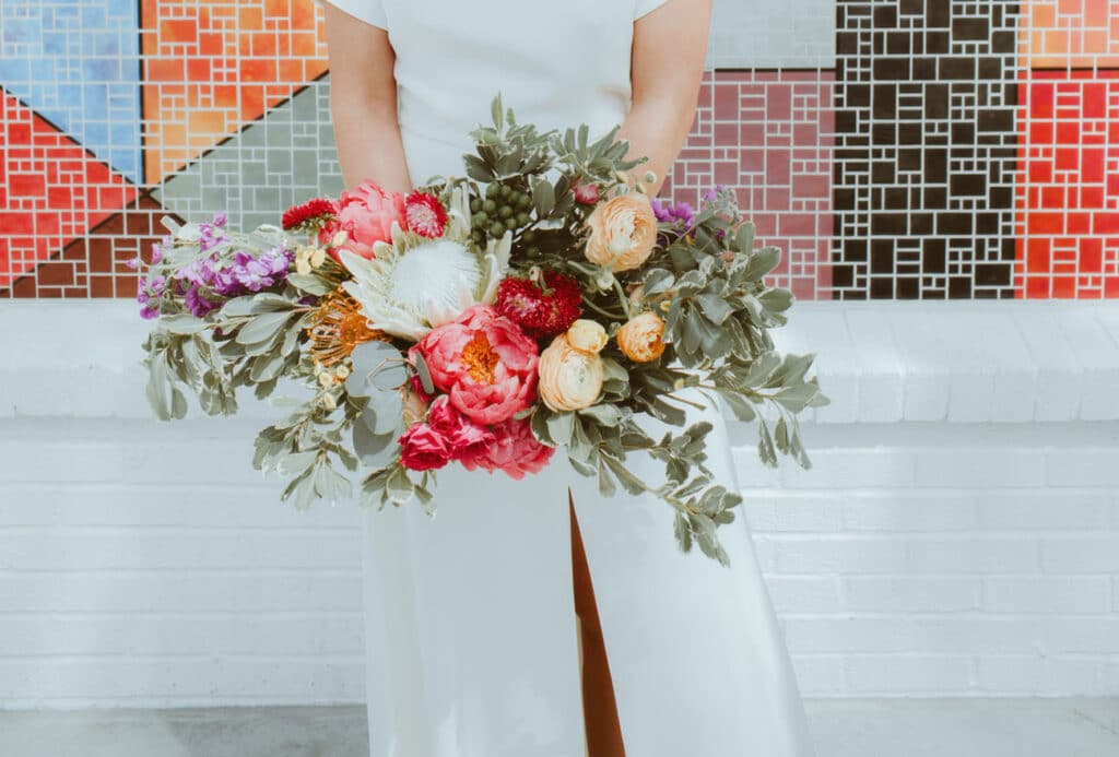 bride with bouquet of reds, yellow and orange against colored tile wall