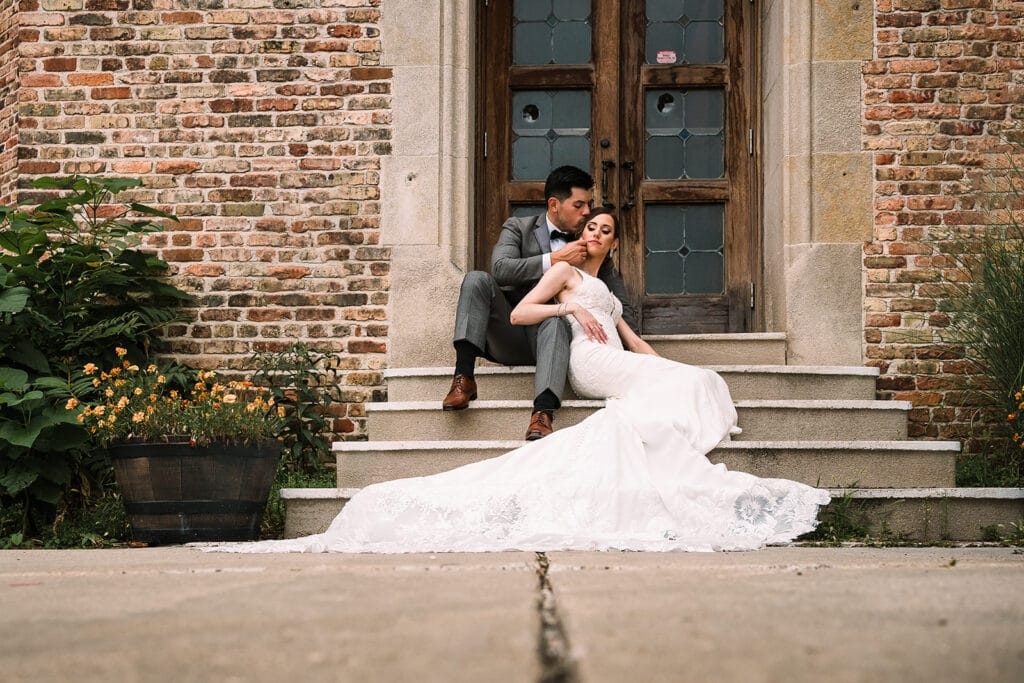 bride and groom sitting on brick stairway to church by Roy Serafin Photo Company
